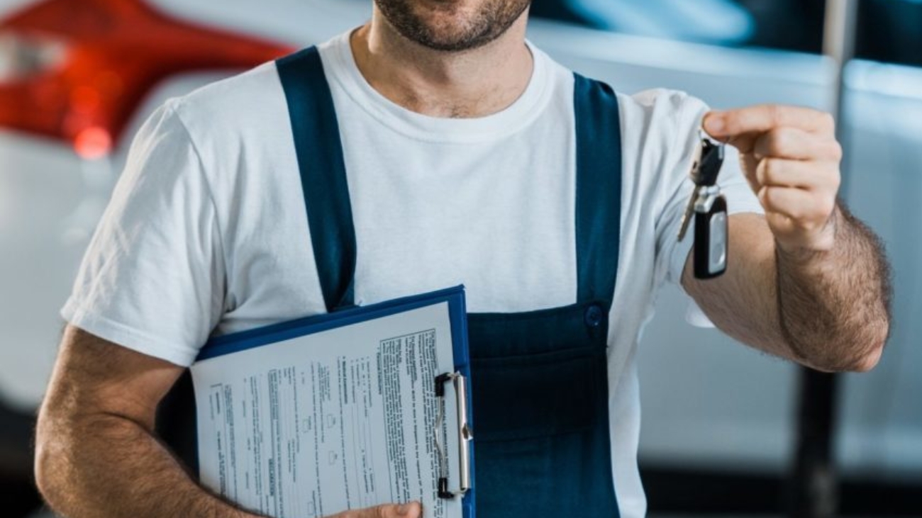 happy-car-mechanic-looking-at-camera-and-holding-clipboard-and-key-near-car-e1651031307472.jpg